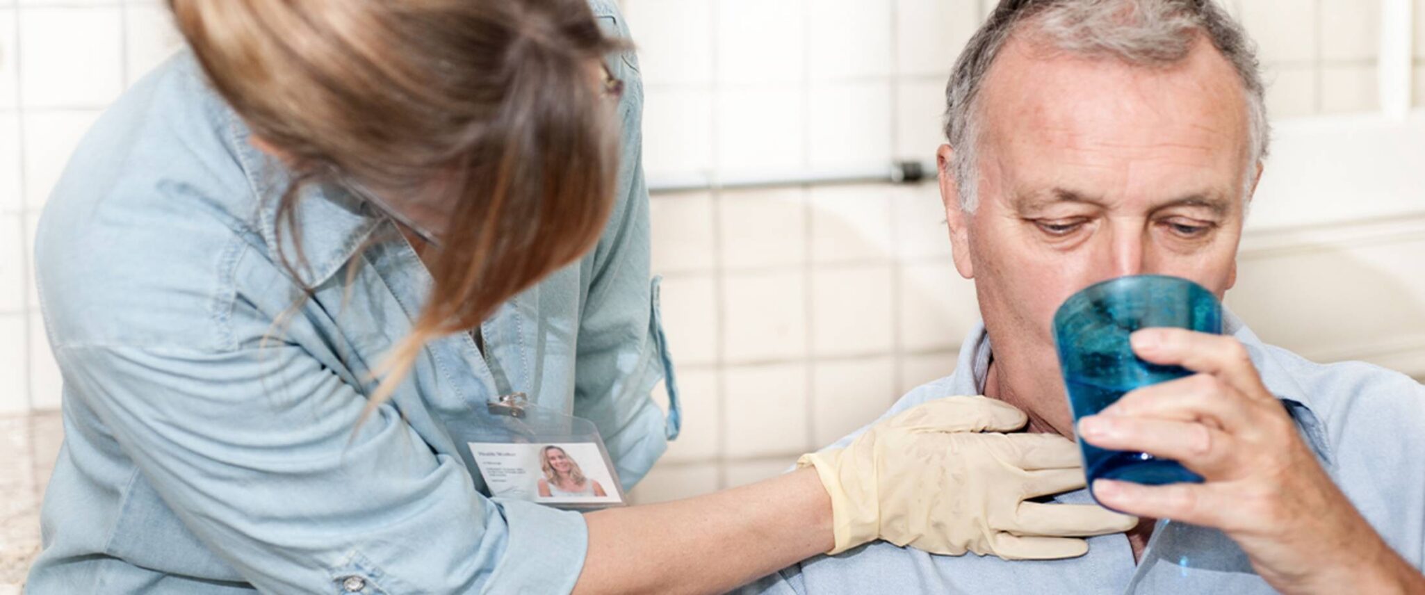 senior drinking water with the assistance of a health care worker