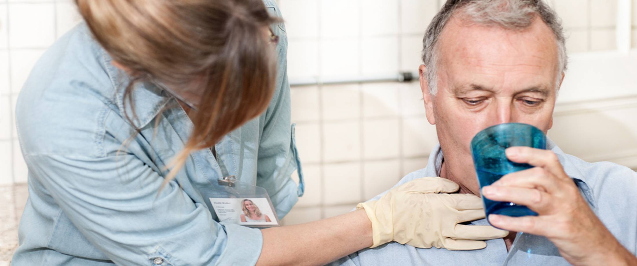 senior drinking water with the assistance of a health care professional