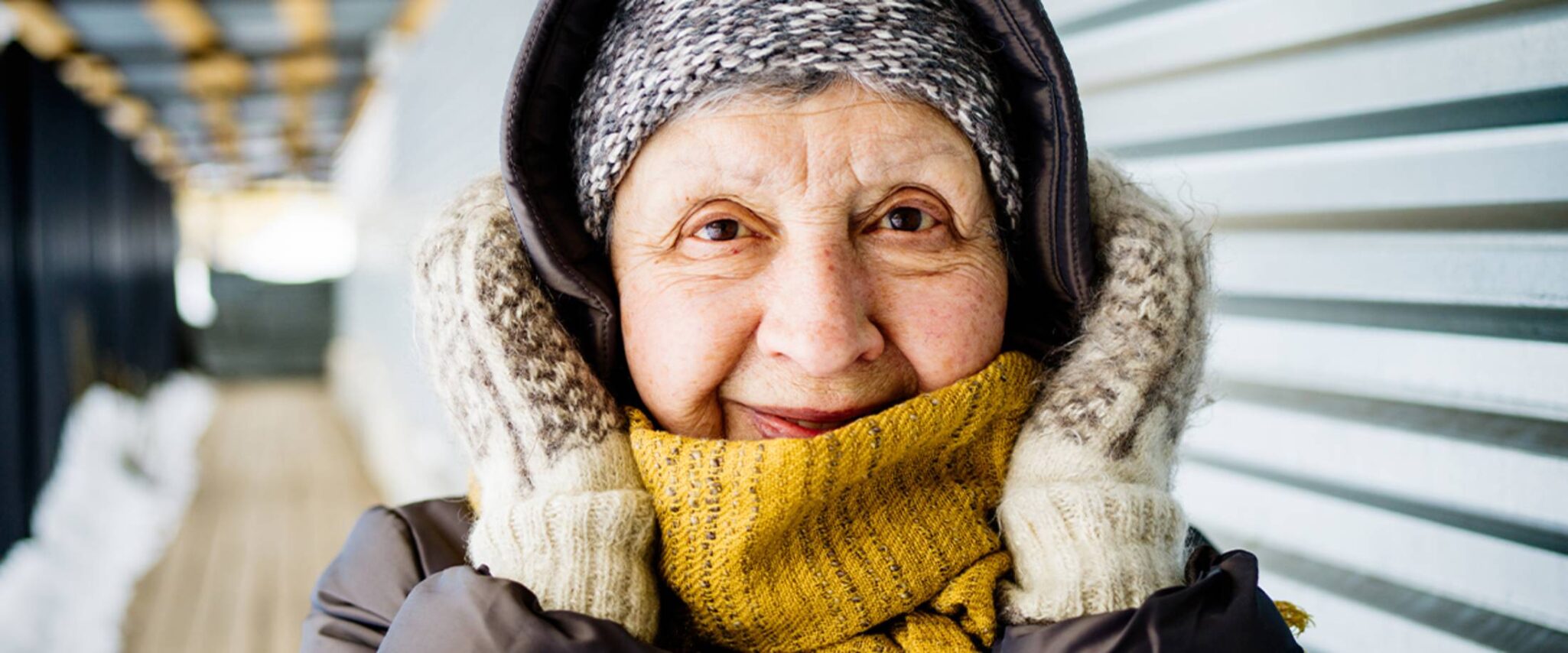 elderly woman covering her ears with her mitten covered hands on a chilly day