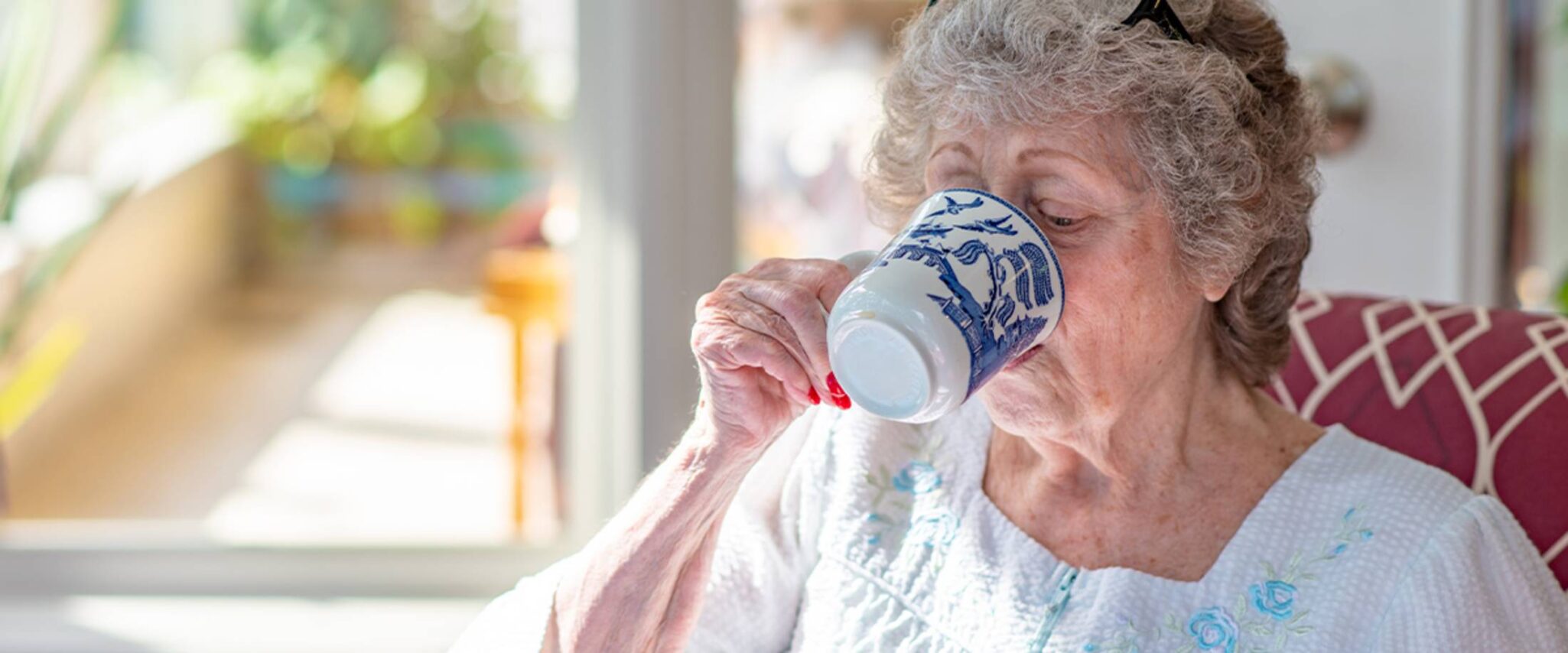 elderly woman drinking a cup of coffee in her night gown
