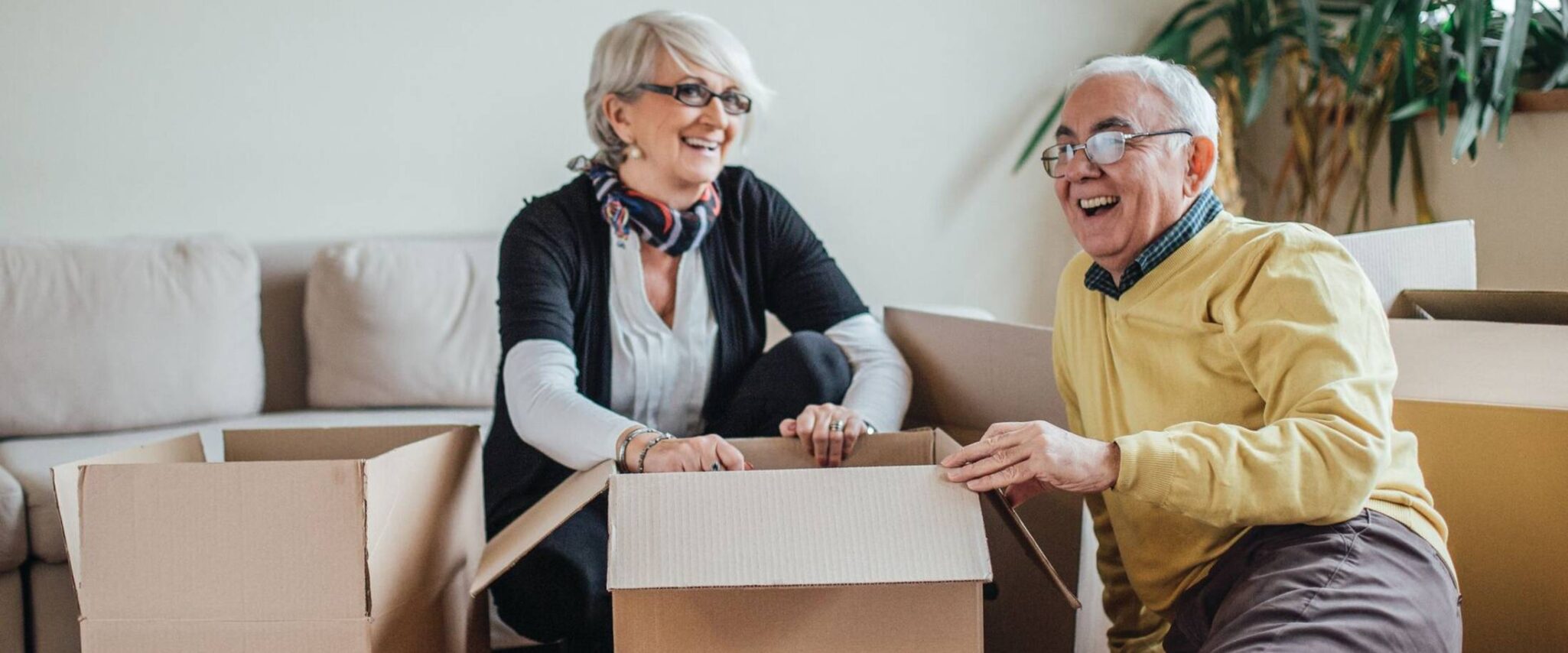 An older man and woman laugh while they pack boxes