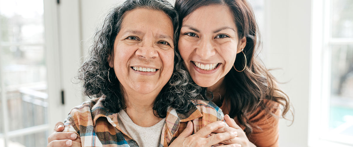 A woman stands behind her elderly mother and they pose for a photo