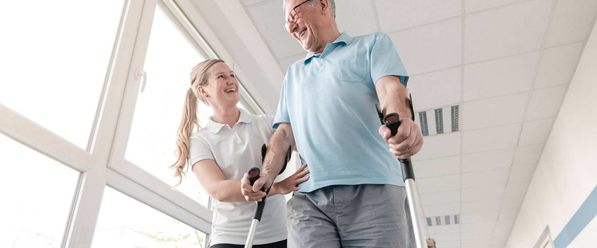 A physical therapist helps an elderly man walk with adaptive equipment