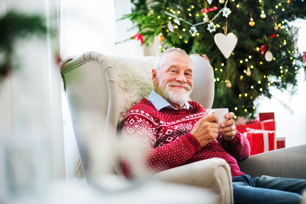 senior man with a cup sitting on armchair at home during Christmas time.