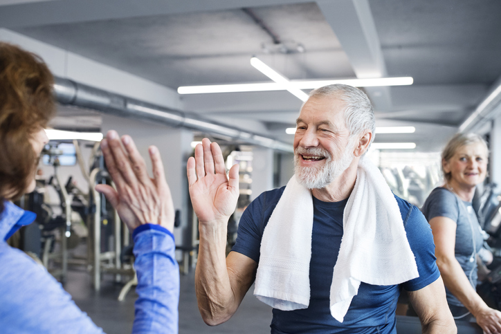 Happy senior man and woman high fiving after working out in gym