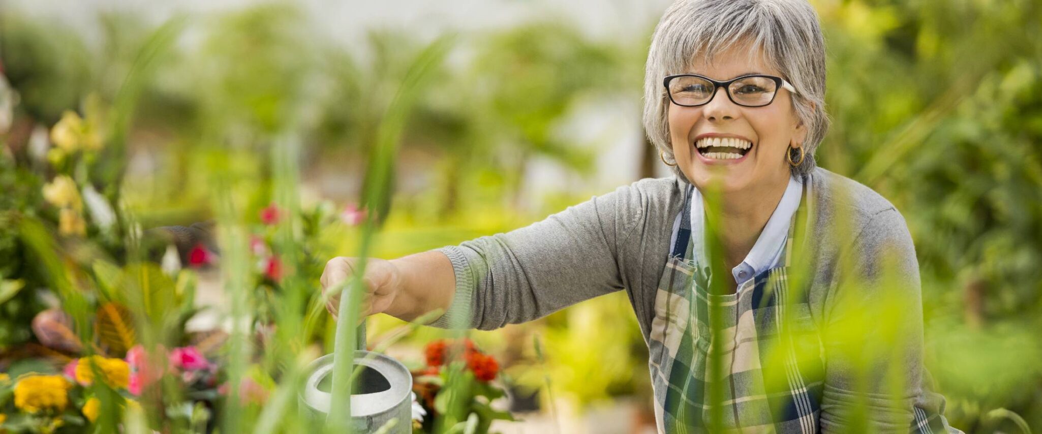 senior watering flowers while smiling at the camera