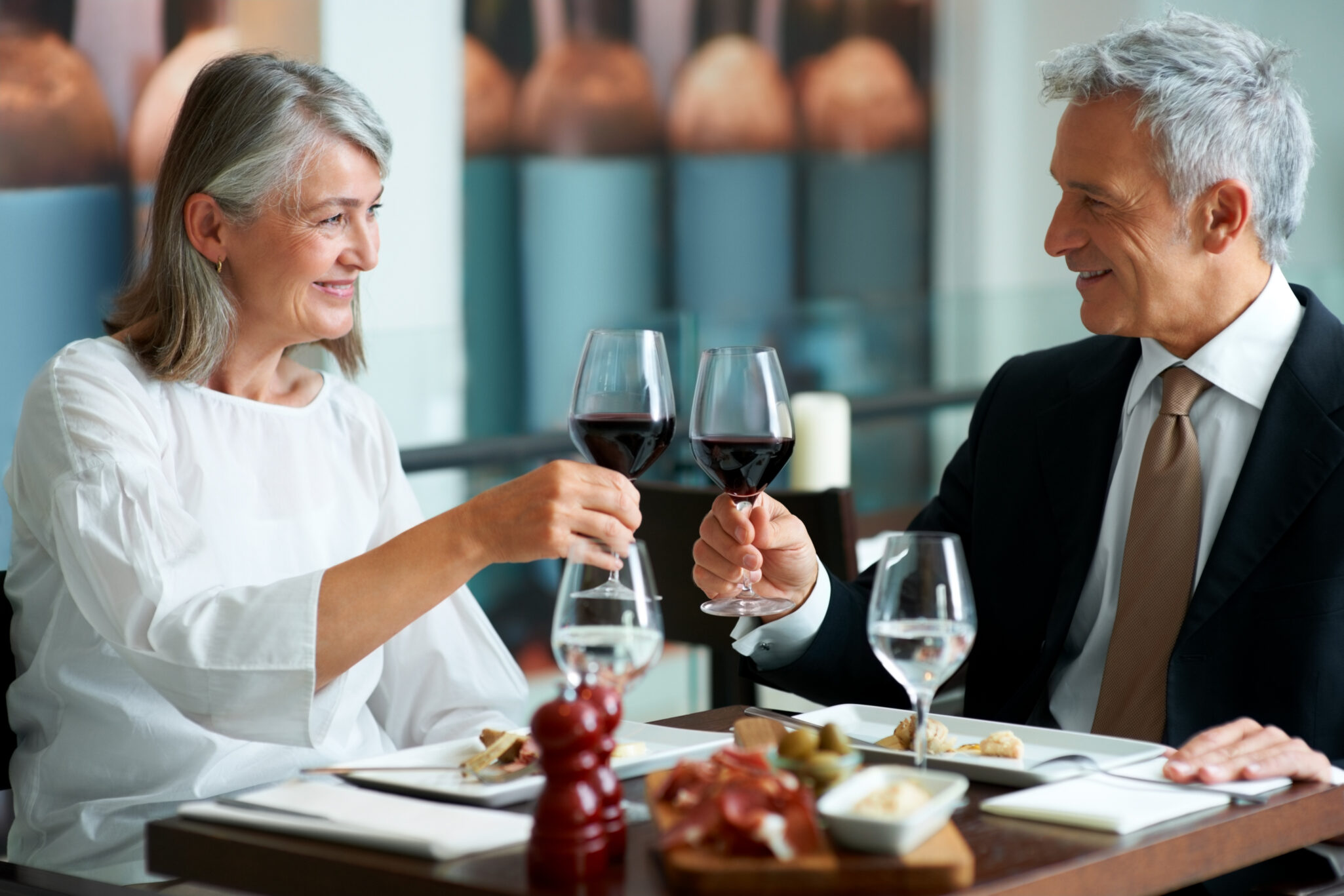 A woman and a man sit down to fine dining and toast with glasses of wine