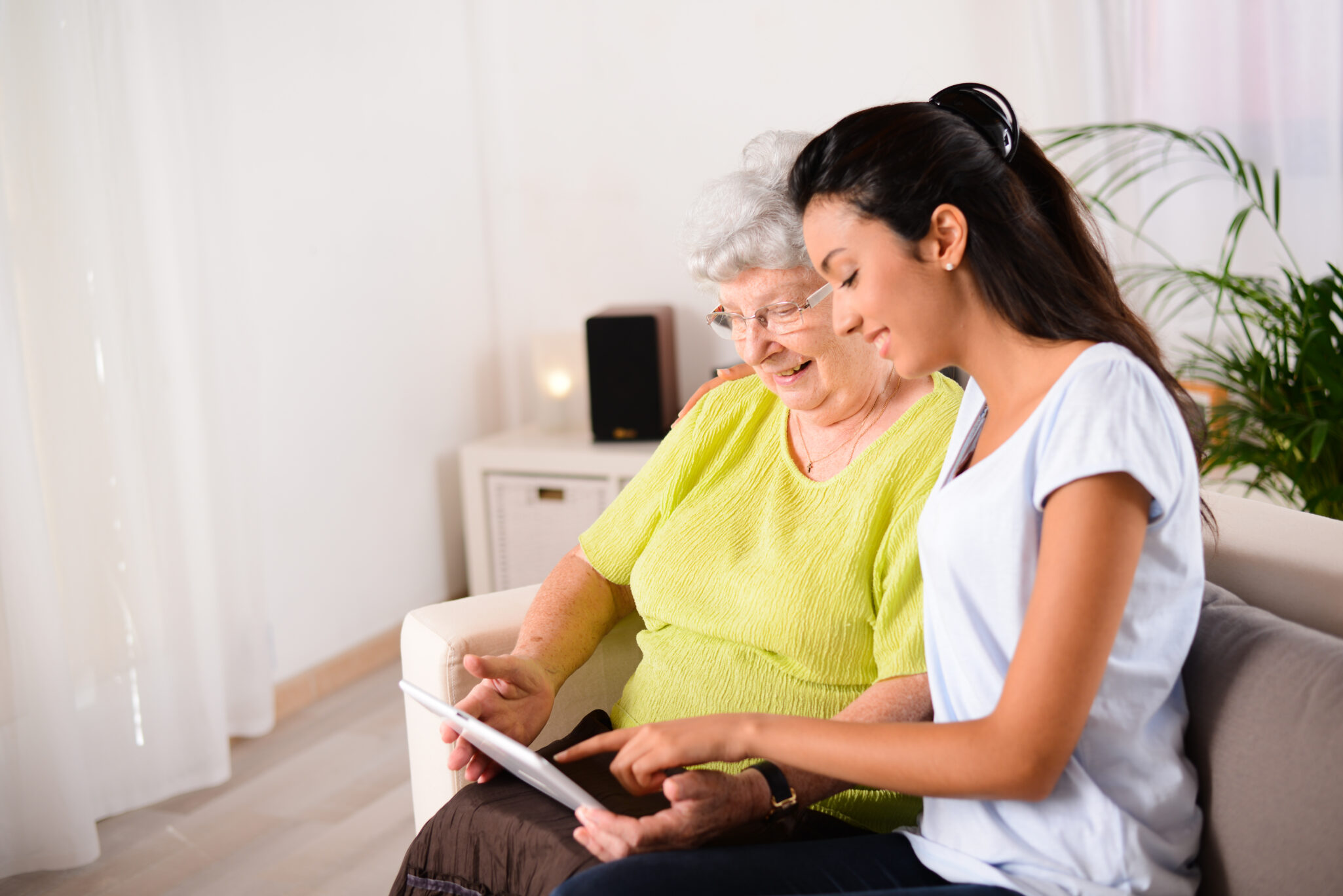 A health care worker sits next to an older woman and points out things on an tablet